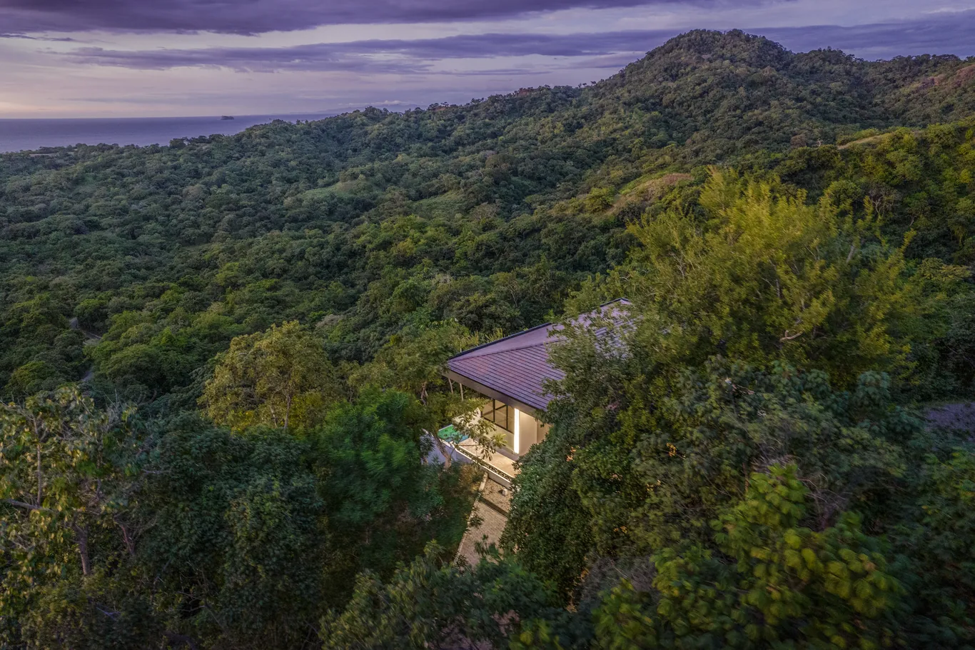 A home in the dry forest canopy at dusk, hills beyond