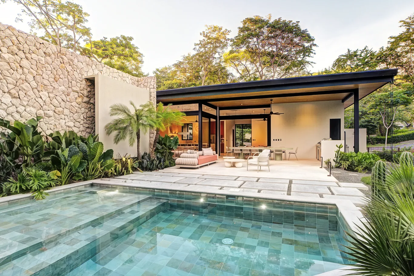 Pool terrace and open living pavilion beside a stone wall