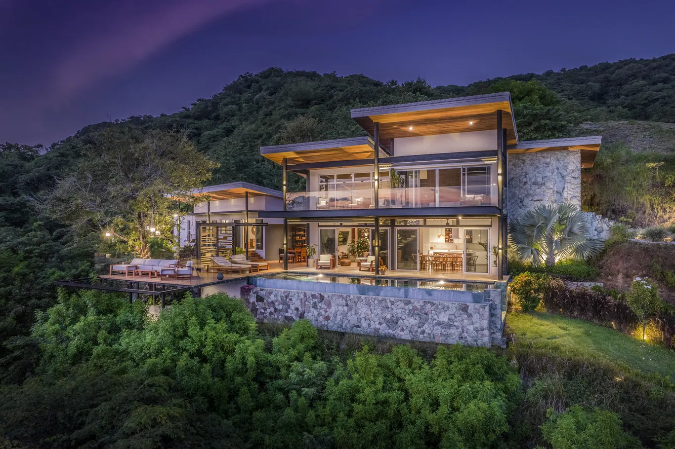 Stone, wood and glass on a hillside elevation at dusk